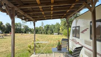 Un espace extérieur abrité, équipé d’une table de pique-nique et de chaises, d’un barbecue, et où un camping-car est stationné à proximité.