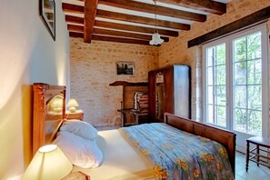 Een slaapkamer met een bed, nachtlampen, een houten hoofdbord, een kledingkast en een raam met uitzicht op groen.