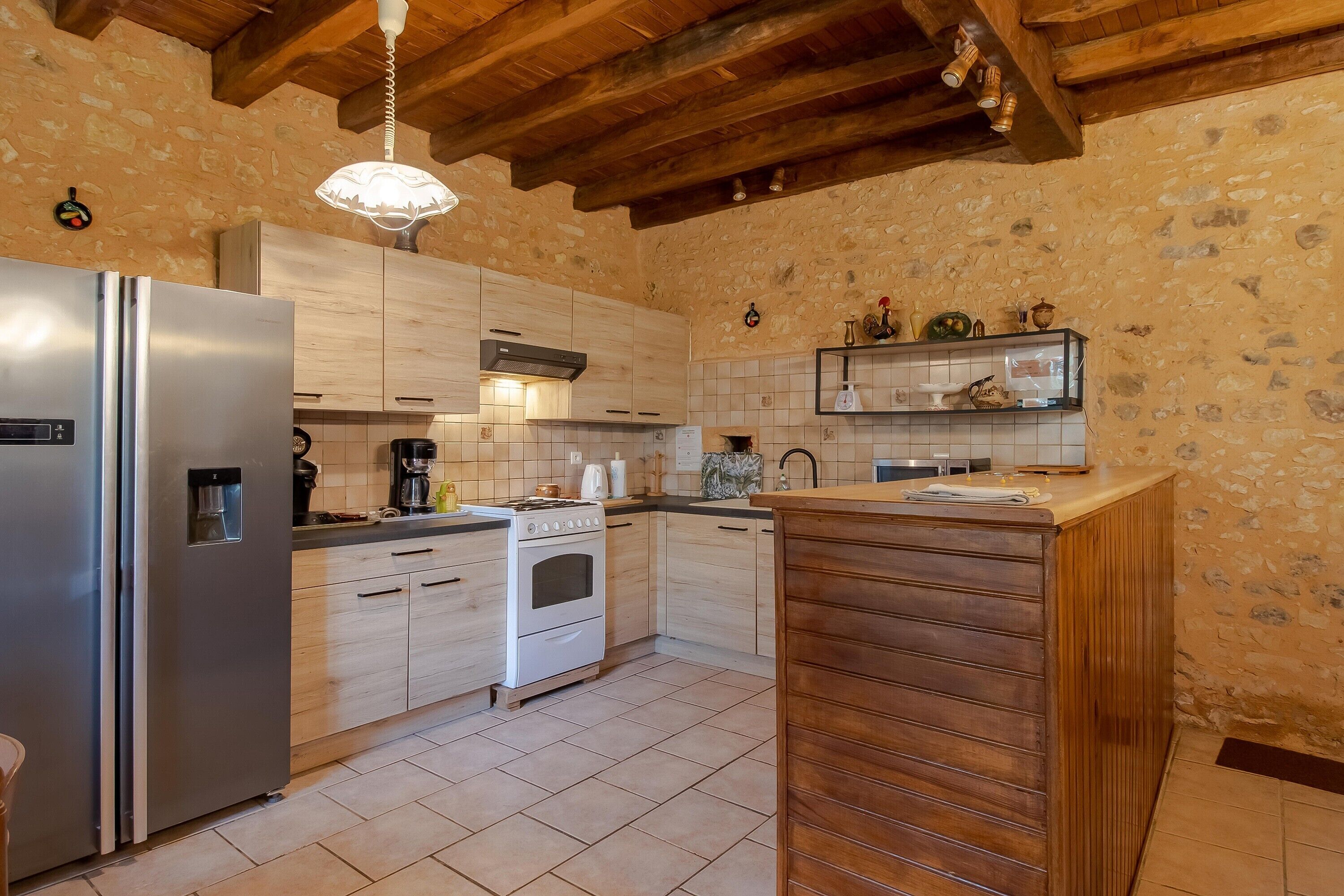 A kitchen with wooden cabinets, a stainless steel refrigerator, a stove, and a hanging light fixture.