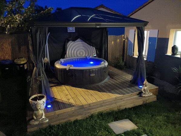 Un jacuzzi bajo un toldo con una terraza de madera, rodeado por una valla y una estatua de Buda.