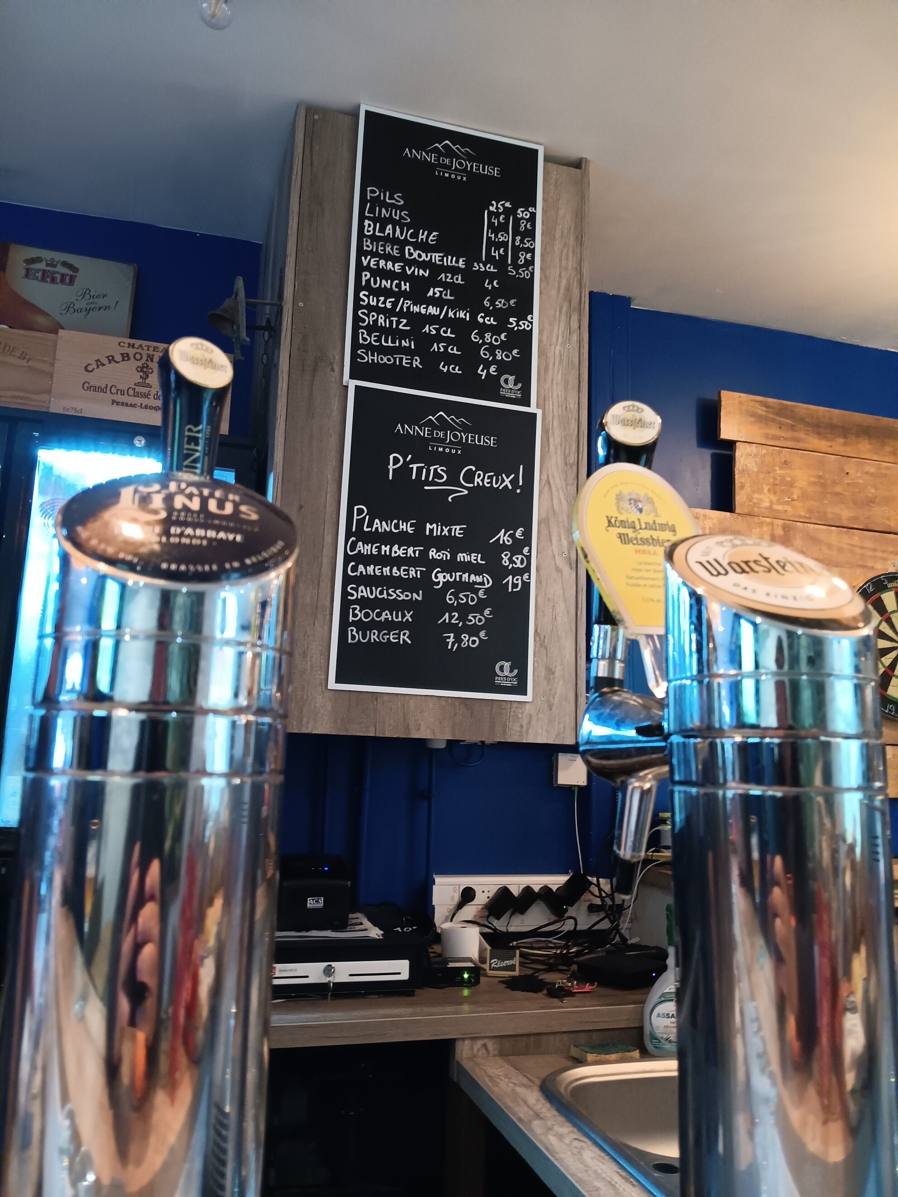A bar area with a chalkboard menu listing various drinks and their prices, a computer, and a sink.