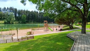 A playground with a slide and swings, a wooden deck, and a lake. - Le Petit Marais – Relaxation for Families with Jacuzzi, Garden, and Air Conditioning (Échiré)