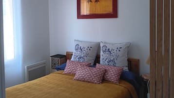 Een slaapkamer met een bed, een hanglamp, een kunstwerk in een lijst en een raam.