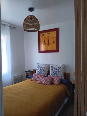 Un dormitorio con una cama, un lámpara colgante, una obra de arte enmarcada y una ventana.