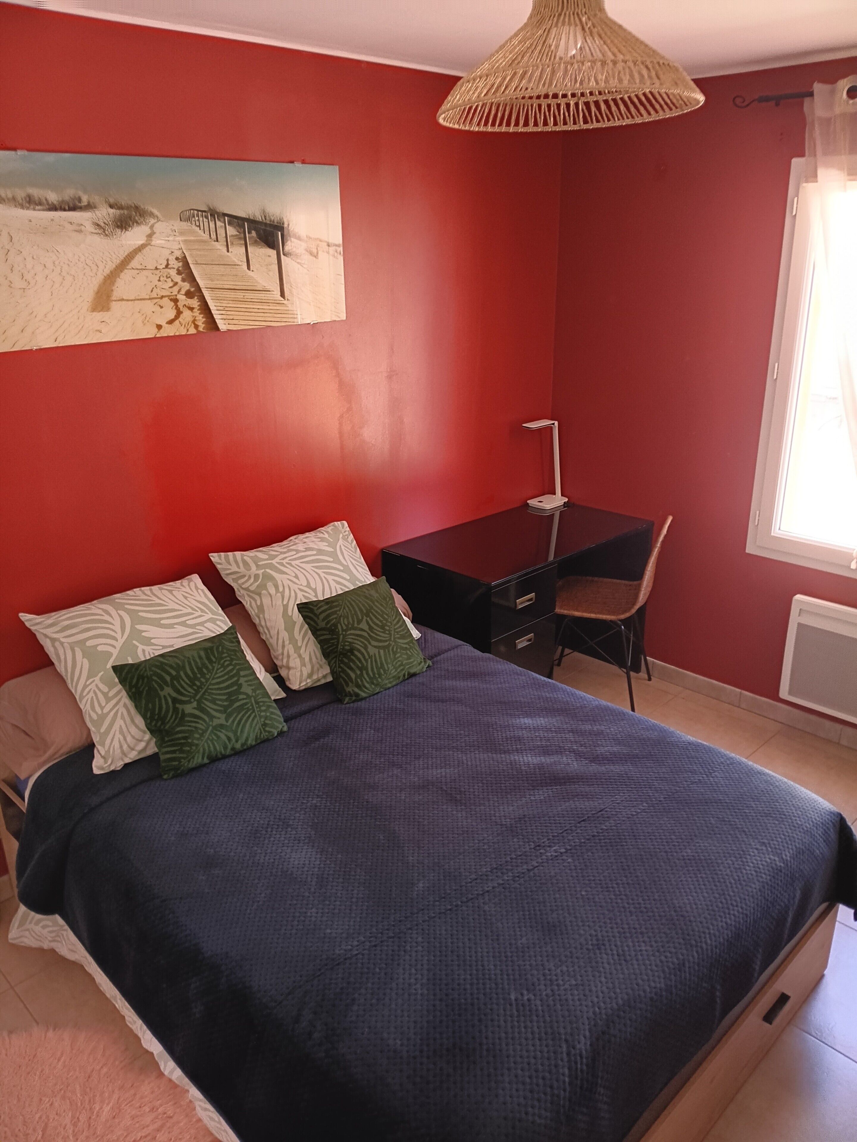 Une chambre à coucher comprenant un lit, un bureau, une chaise, un luminaire suspendu et une fenêtre.