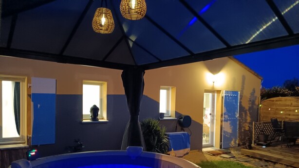A hot tub under a covered patio with a view of a house and a garden. - Le Petit Marais – Relaxation for Families with Jacuzzi, Garden, and Air Conditioning (Échiré)