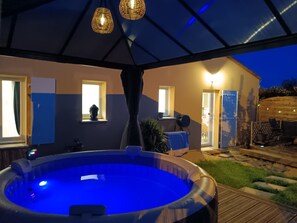 A hot tub under a covered patio with a view of a house and a garden.