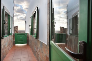 Un pasillo estrecho con puertas y ventanas verdes, paredes de piedra y suelo de baldosas.