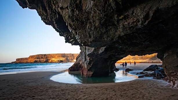 A beach with a large rock formation, calm water, and distant cliffs. - Holiday Home 'Casa Dayaday' with Mountain Views and Wi-Fi (Puerto del Rosario)