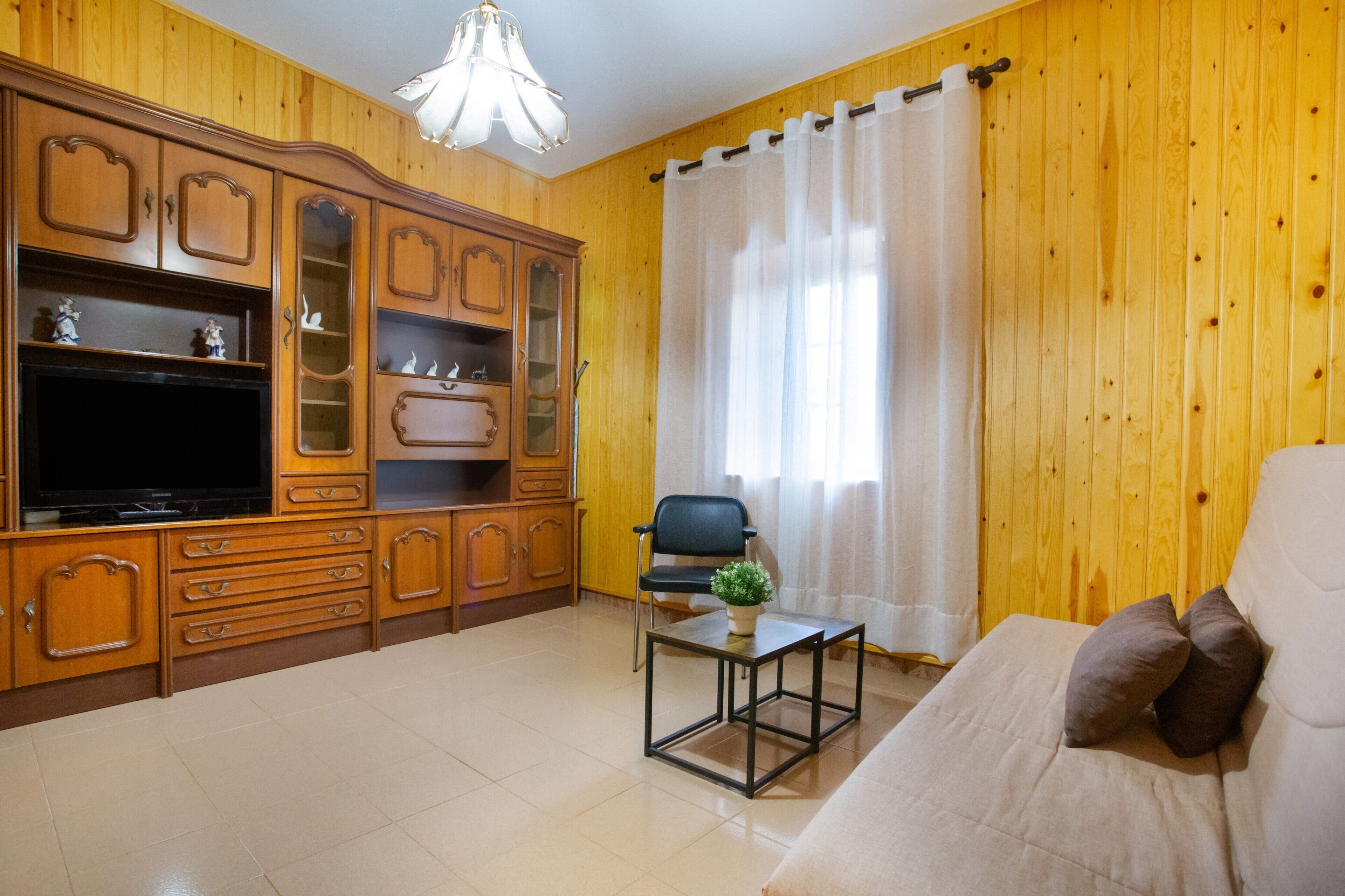 A living room with wooden paneling, a sofa, a TV stand, and a chair.