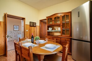 Un comedor con una mesa de madera dispuesta para cuatro, un armario empotrado de madera con puertas de cristal y un refrigerador de acero inoxidable.