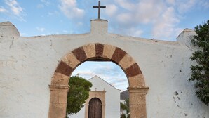 A white building with a cross on top, an archway, and a small church in the background. - Holiday Home 'Casa Dayaday' with Mountain Views and Wi-Fi (Puerto del Rosario)