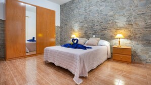 A bedroom with a stone wall, a wooden wardrobe, a bed with a quilt, and bedside lamps. - Holiday Home 'Casa Dayaday' with Mountain Views and Wi-Fi (Puerto del Rosario)