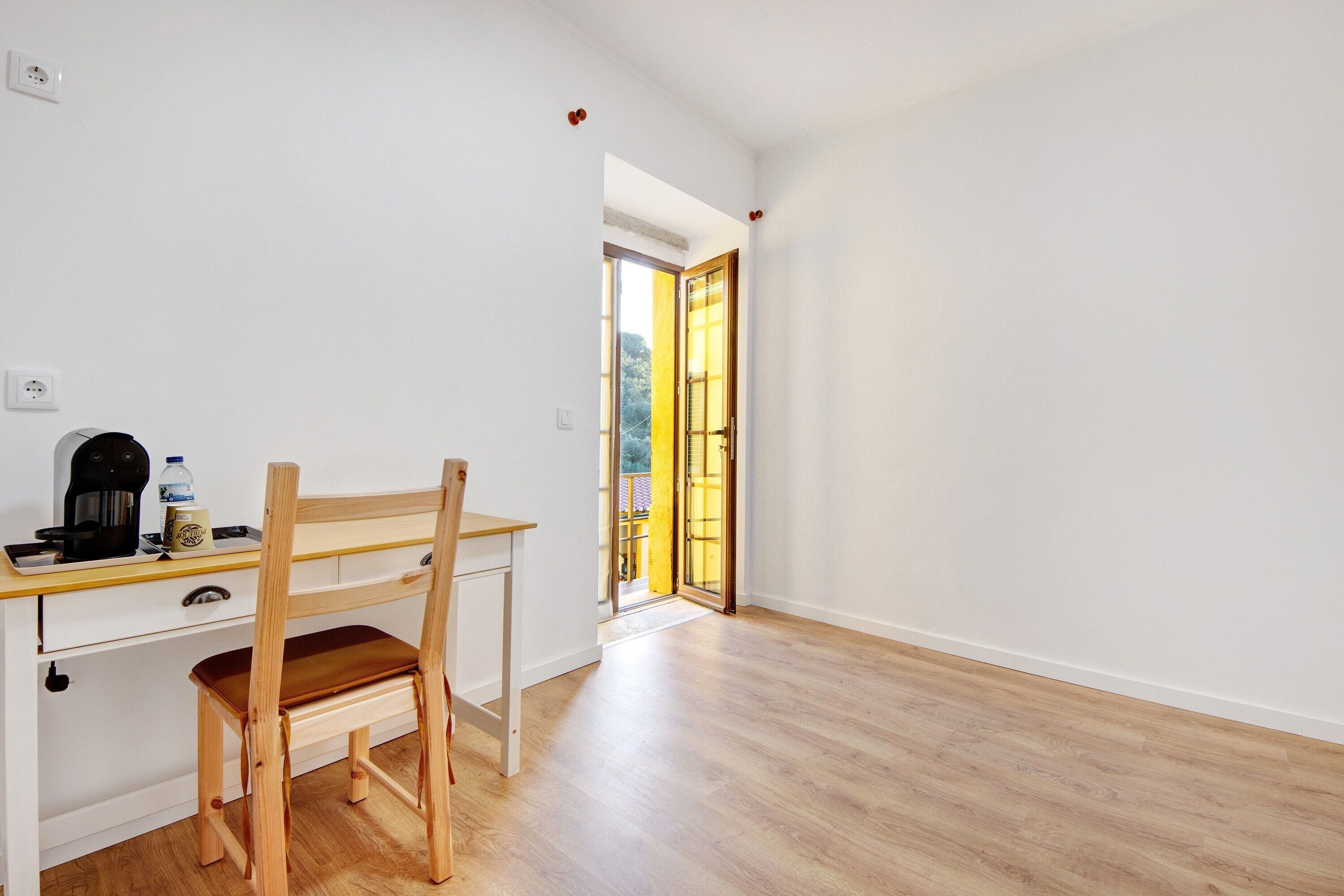 Una habitación con un escritorio de madera, una silla y vistas a través de una puerta abierta.
