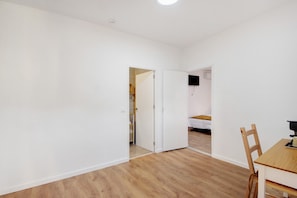 Ein Zimmer mit Holzboden, weißen Wänden, einem Holztisch mit Stühlen und einem Bett im Hintergrund.