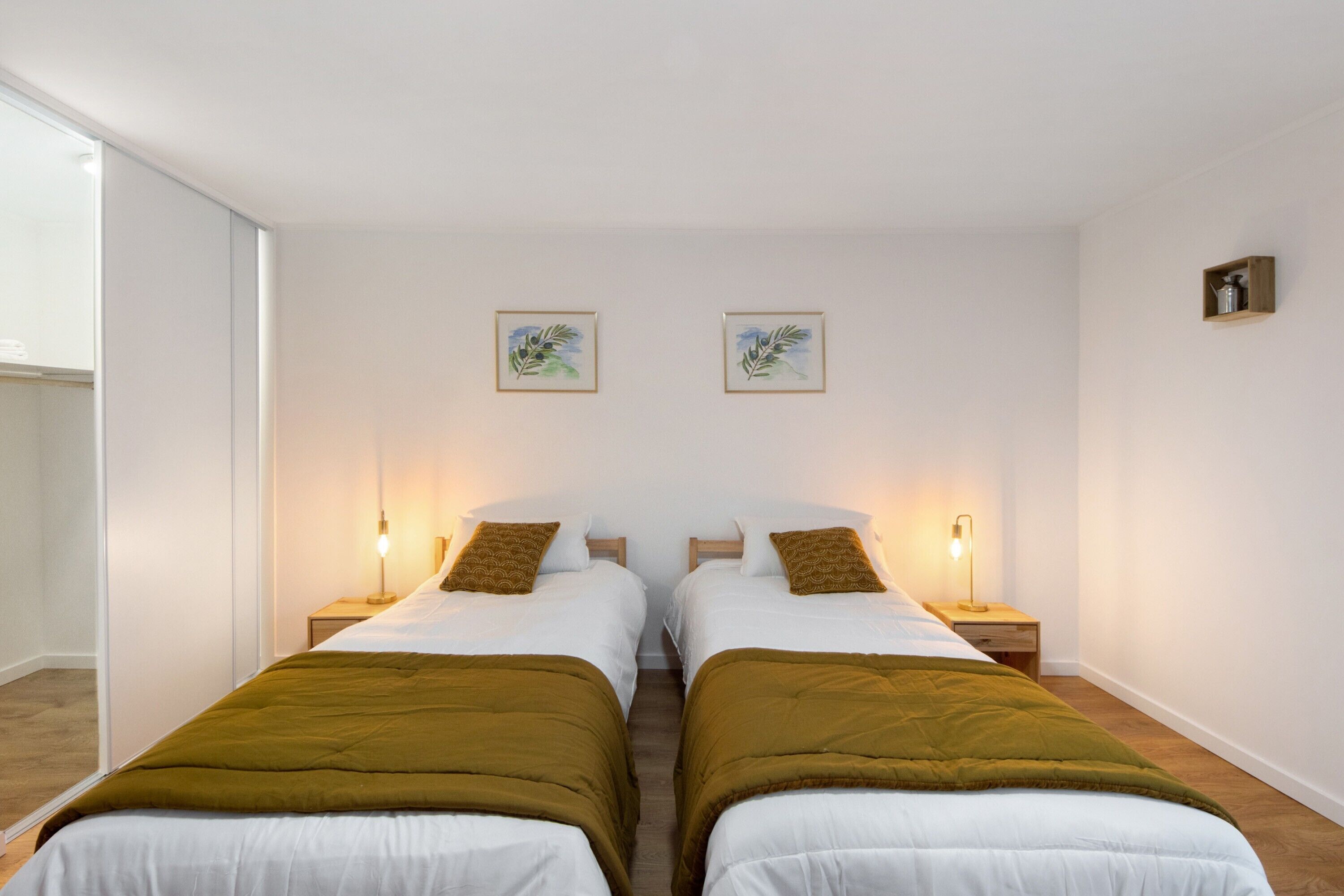 Une chambre avec deux lits simples, des lampes de chevet et des œuvres d’art encadrées accrochées au mur.