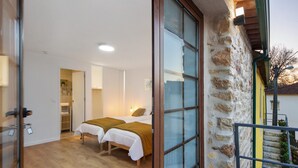 Ein Zimmer mit zwei Betten, Holzboden, Steinwand und Glastür zum Außenbereich.