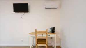Ein Zimmer mit einem Holztisch, einem Stuhl, einem an der Wand befestigten Fernseher und einer Klimaanlage.