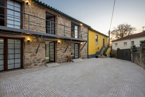 A stone building with a balcony, a yellow wall, and a paved courtyard. - Room 'Quarto 3 Piso Superior - Quinta Df' with Mountain View, Wi-Fi and Air Conditioning (Coimbra)