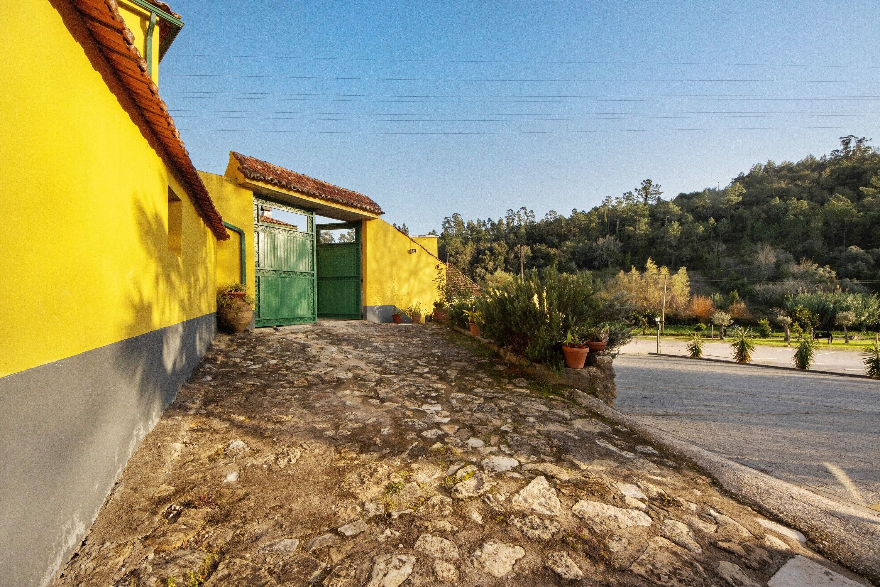 Un edificio giallo con una porta verde, un vialetto in pietra e un pendio boscoso sullo sfondo.