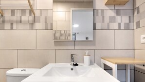 Een badkamer met een witte wastafel, een spiegel, een toilet en een houten tafeltje.