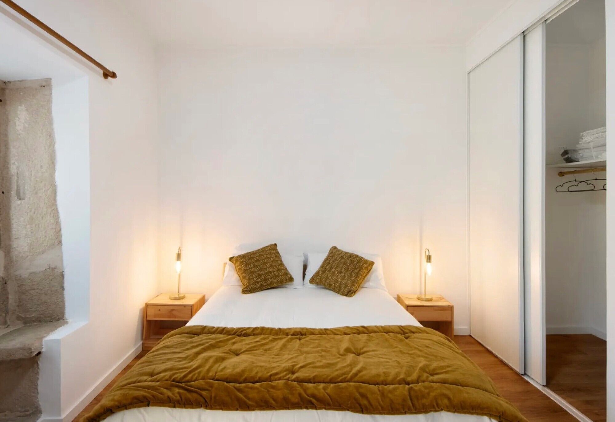 A bedroom with a bed, two bedside lamps, a wooden nightstand, a brown blanket, and a closet with a mirror.