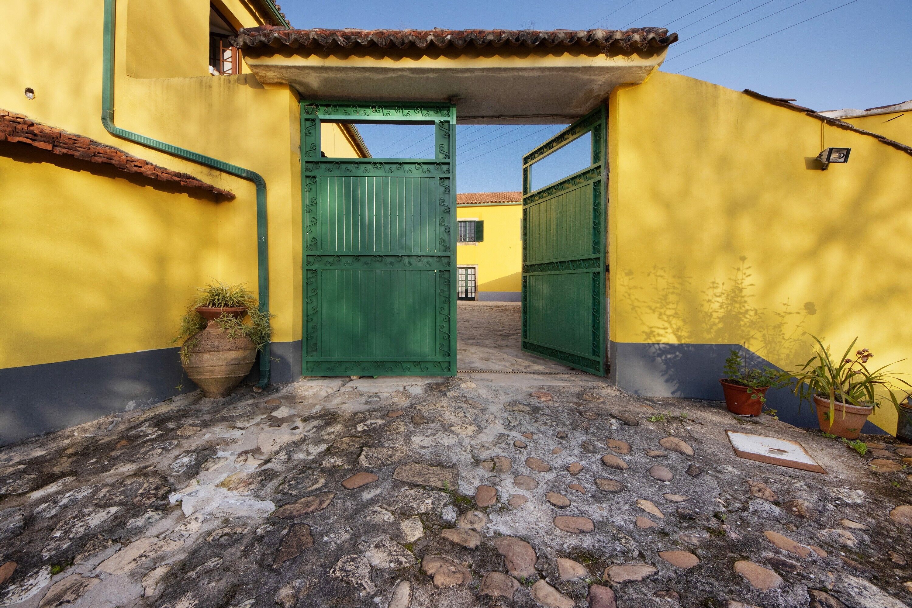 Une ruelle étroite avec un bâtiment jaune, des portails verts et des plantes en pot.