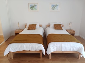 Deux lits simples avec des cadres en bois, du linge de lit blanc et des plaids marron. Chaque lit est muni d’une table de chevet avec une lampe.