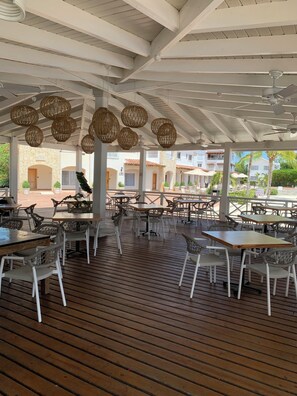An outdoor dining area with wicker hanging lights, white chairs, and tables.
