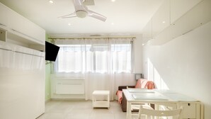 A bright room with a ceiling fan, a window with sheer curtains, a small white table, and a bed with pink bedding.