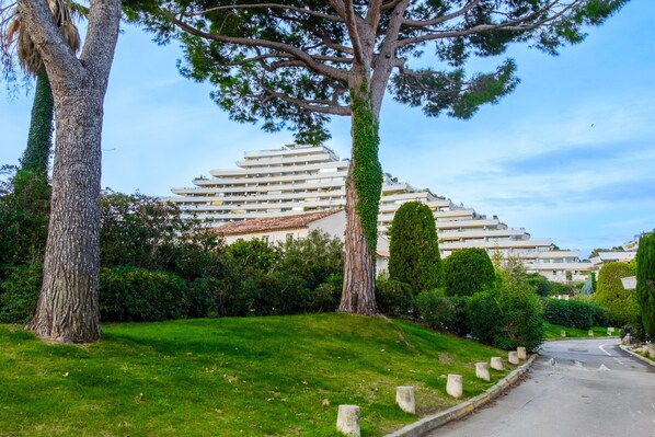 Un edificio residencial de diseño moderno, rodeado de vegetación cuidada y un cielo despejado.