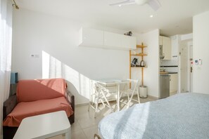 Una habitación compacta con cama, sofá, una mesita, escritorio y kitchenette.