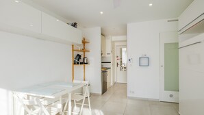 A modern kitchen with white cabinetry, a dining area with a table and chairs, and a hallway leading to a door.