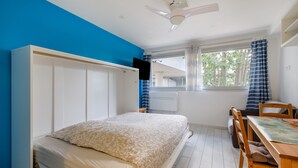 A bedroom with a bed, a desk, a chair, a ceiling fan, and a window with curtains. - Studio Apartment 'Enjoy French Riviera - Fame Marina' with Wi-Fi and Air Conditioning (Villeneuve-Loubet)