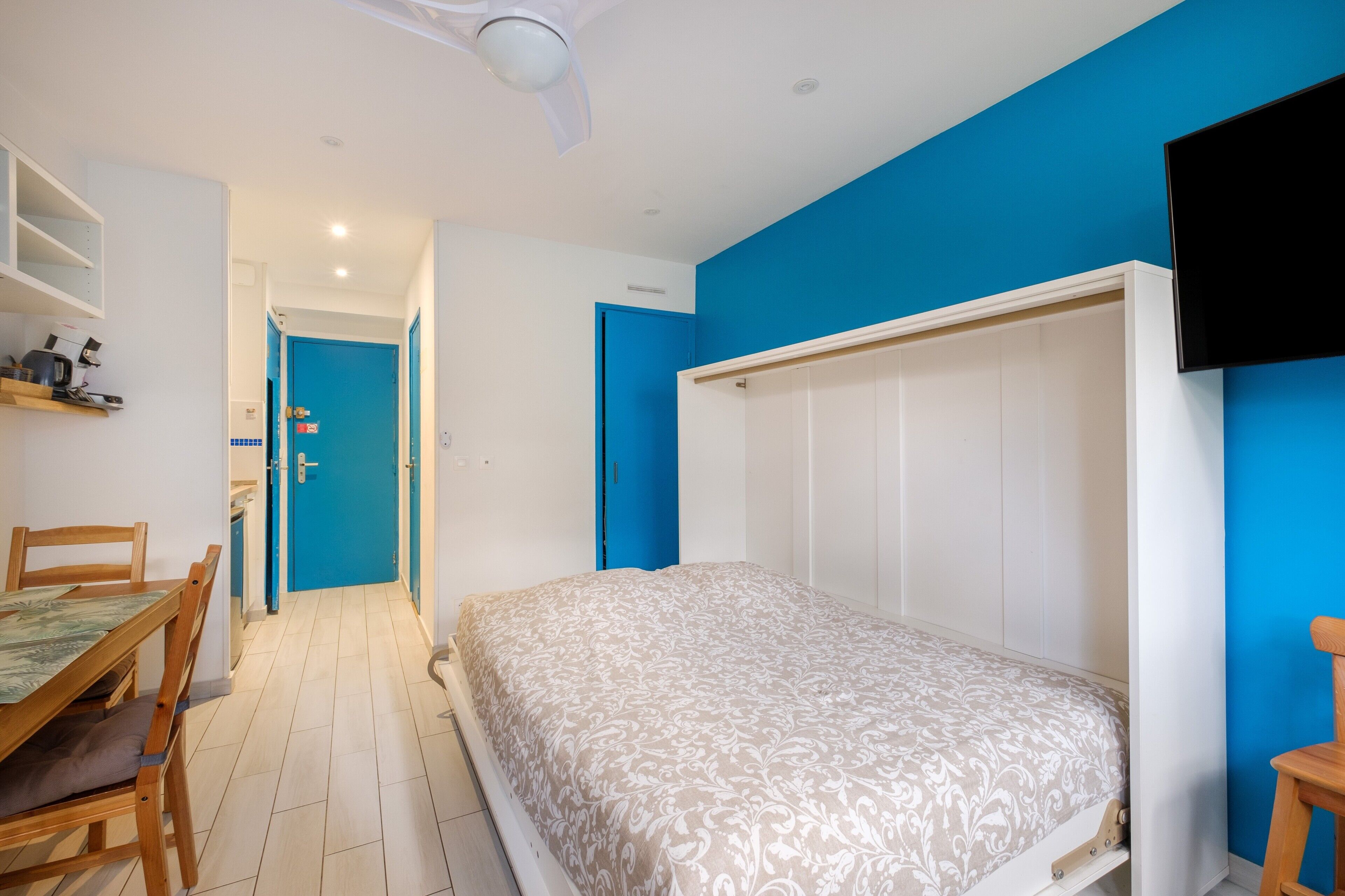 Une chambre à coucher avec un lit, un bureau avec des chaises, une armoire et un téléviseur fixé au mur.
