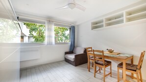 A modern kitchen with white cabinetry, a dining area with a wooden table and chairs, a ceiling fan, and a view of greenery outside. - Studio Apartment 'Enjoy French Riviera - Fame Marina' with Wi-Fi and Air Conditioning (Villeneuve-Loubet)