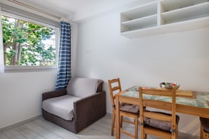 Una habitación con sofá, una mesa de comedor con sillas, un ventanal con cortinas y una pared blanca con estante.