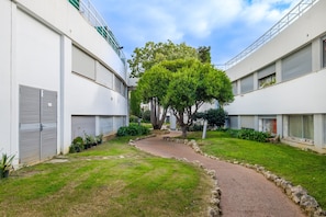 Un patio con un árbol en el centro, un camino de grava y edificios blancos con contraventanas cerradas.