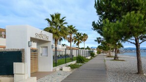Un chemin menant à un bâtiment portant l’inscription « SYRACUSE », avec vue sur la plage et les palmiers.