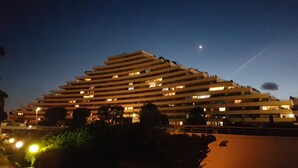 Un hôtel à plusieurs étages doté d’une architecture originale en terrasses, de fenêtres illuminées et d’un croissant de lune dans le ciel.