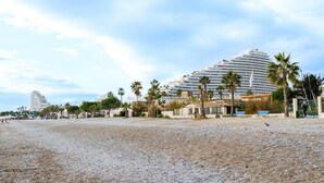A beach with a large hotel, palm trees, and a pebbled walkway. - Studio Apartment 'Venus - Rdc - 2 Couchages Doubles' with Wi-Fi and Air Conditioning (VILLENEUVE LOUBET)