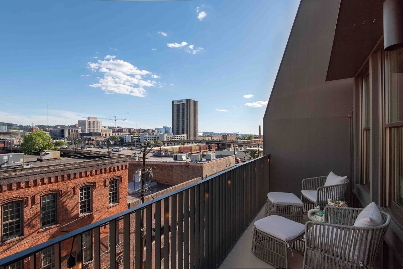 A balcony with wicker chairs, a view of a cityscape including a tall building labeled 'BBVA,' and a brick building in the foreground.