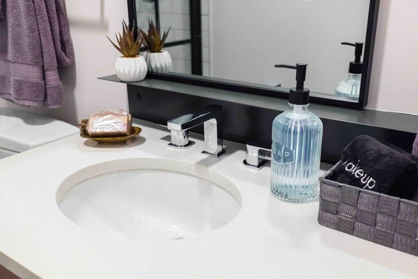 Un lavabo con espejo, dispensador de jabón, una botella de jabón líquido y un perchero para toallas.