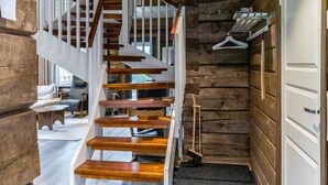 A wooden staircase with white railings leading to a room with a wooden wall and a coat rack.