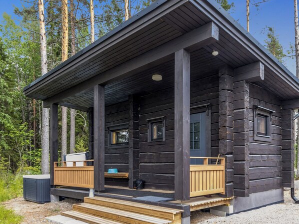 A log cabin with a porch, wooden steps, and a window.