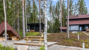 A cabin with a wooden deck, surrounded by tall pine trees.