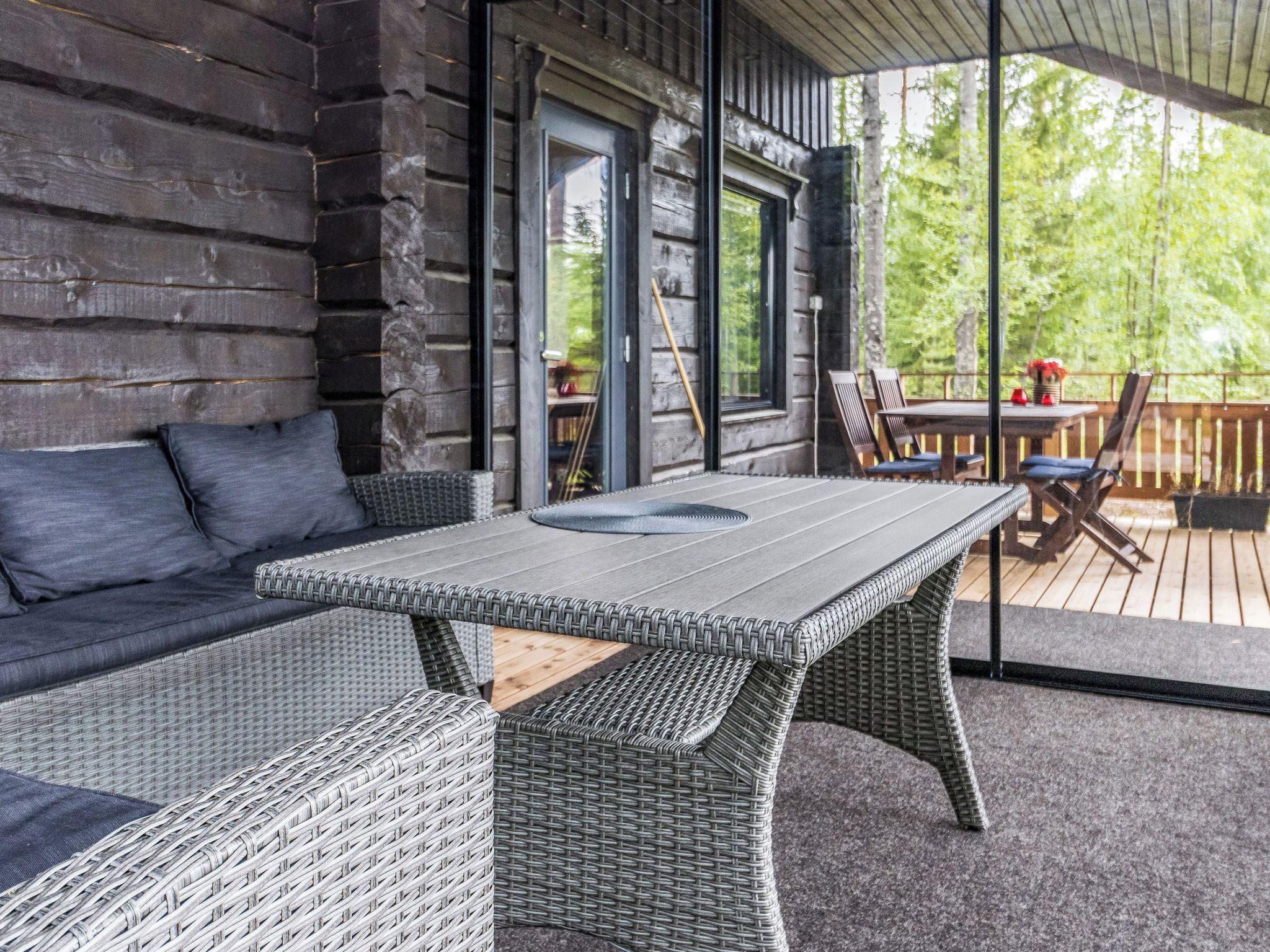 A wooden cabin with a covered porch, a wicker sofa, a dining table, and chairs.