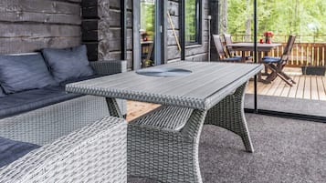 A wooden cabin with a covered porch, a wicker sofa, a dining table, and chairs.