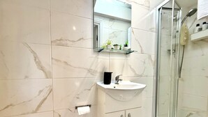 A bathroom with a glass shower enclosure, a white sink, and a marble-tiled wall.
