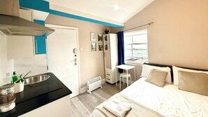 A compact hotel room with a kitchenette, a bed, a desk, and a window with a city view.
